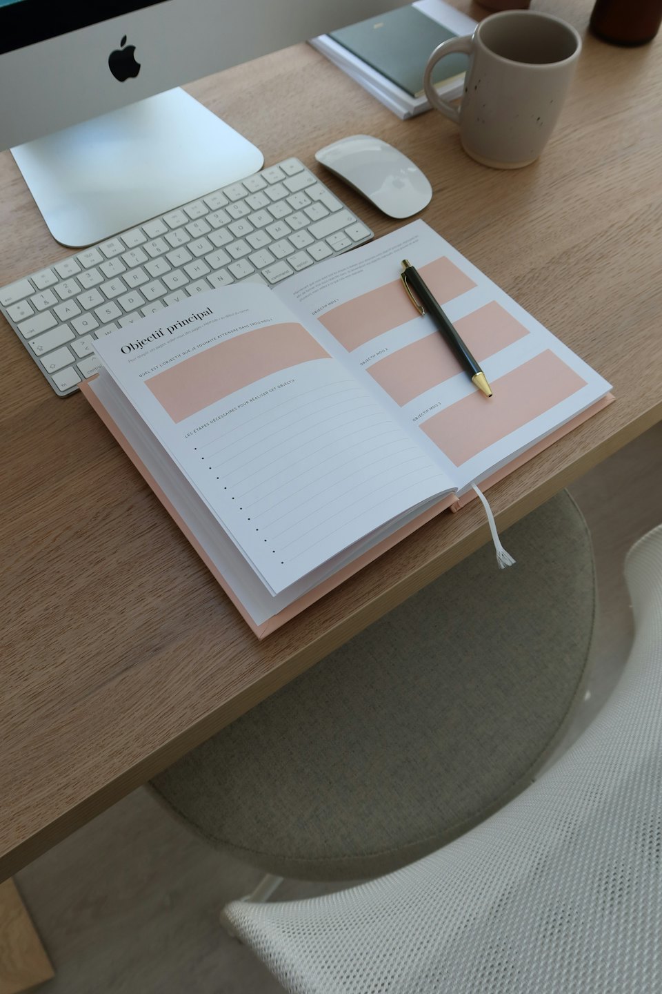 An open planner and pen sit on a wooden office desk.