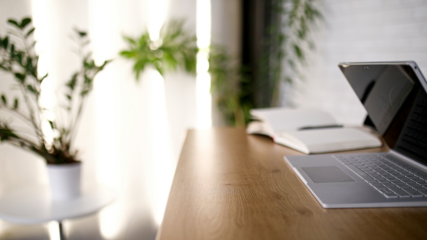A silver laptop rests on a wooden desk with a notebook.