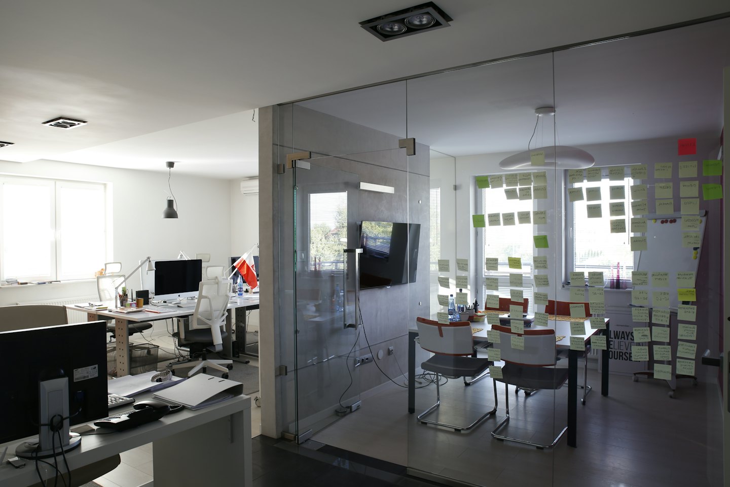 Modern office with a meeting room covered in yellow and green post-it notes.